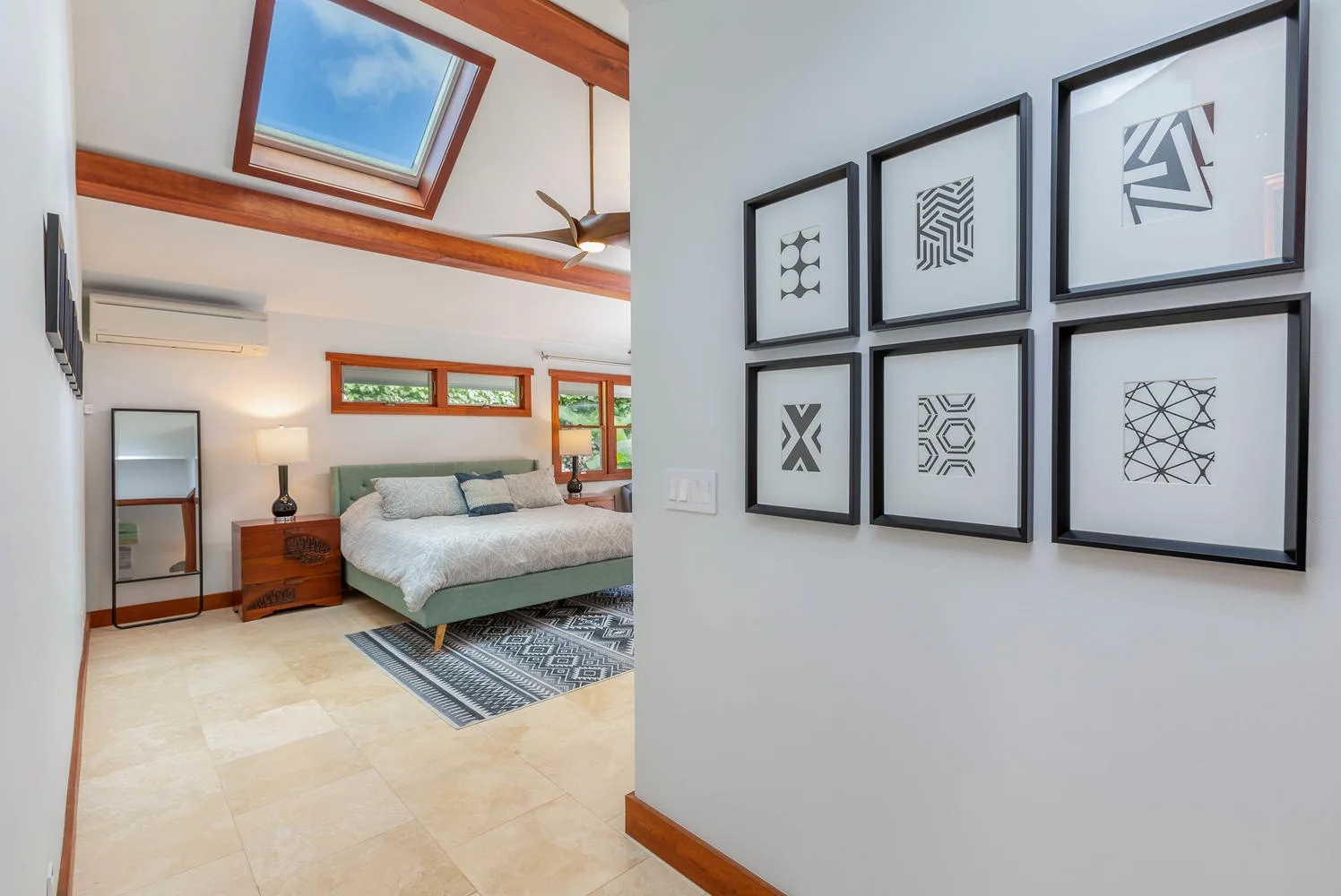A bedroom with a bed beneath a skylight and framed geometric artwork on the wall.