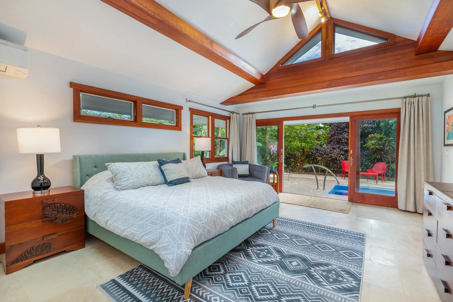 A bright bedroom with a large bed, exposed wooden beams, and glass doors opening to a patio.