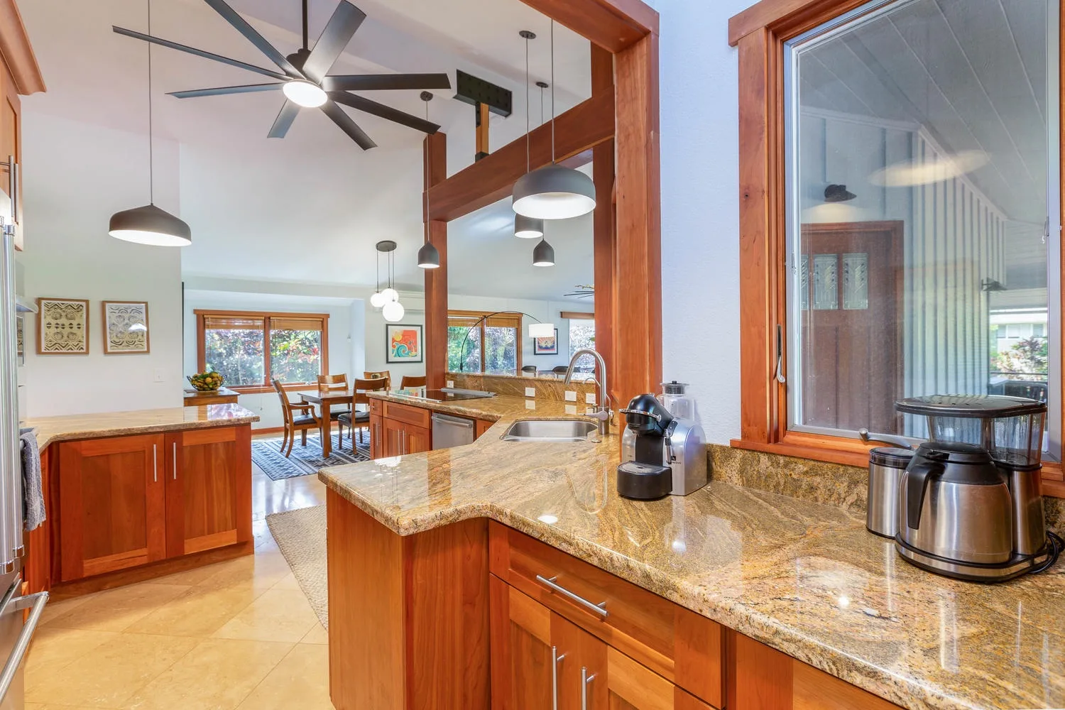 A kitchen with wood cabinetry and a stone countertop opens onto a dining area.