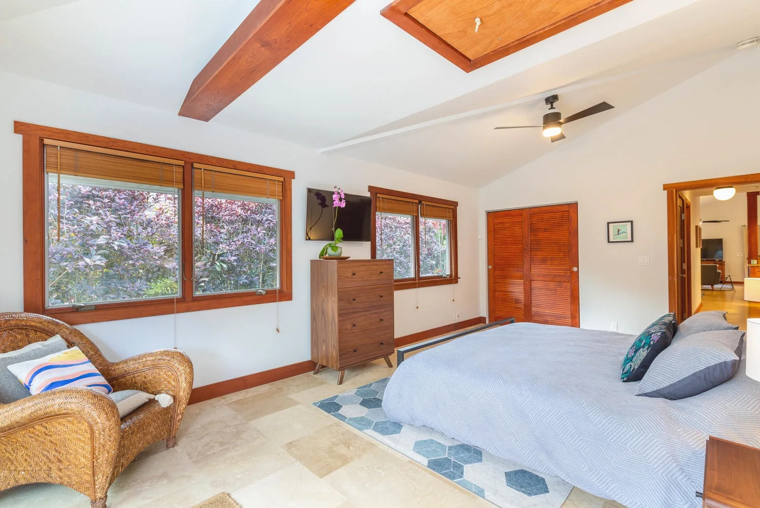 A bright bedroom with a large bed, wooden furnishings, and broad windows.