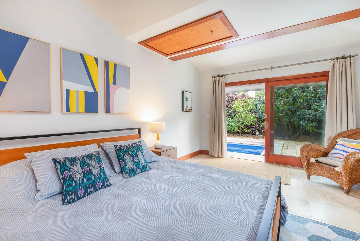 A bright bedroom with a large bed and sliding glass doors opening onto a garden.