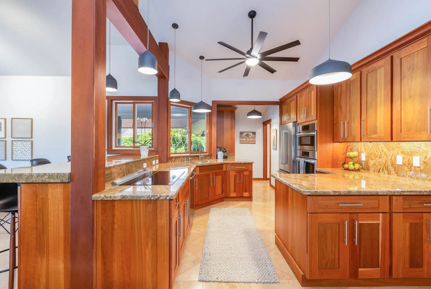 A spacious kitchen with wood cabinetry, stone countertops, and a ceiling fan.