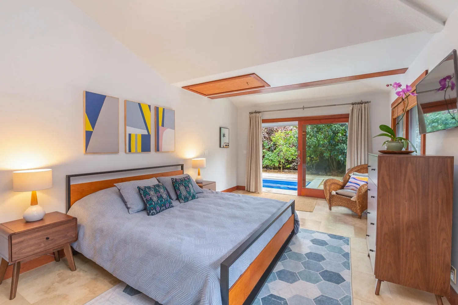 A bedroom with a large bed, bedside tables, and sliding glass doors opening to greenery.