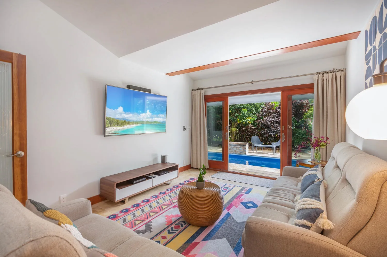A bright living room with seating, a colorful rug, and glass doors opening to a patio.