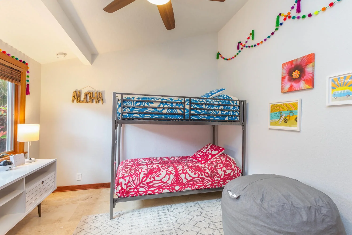 A bright bedroom with a metal bunk bed, colorful bedding, and wall decorations.
