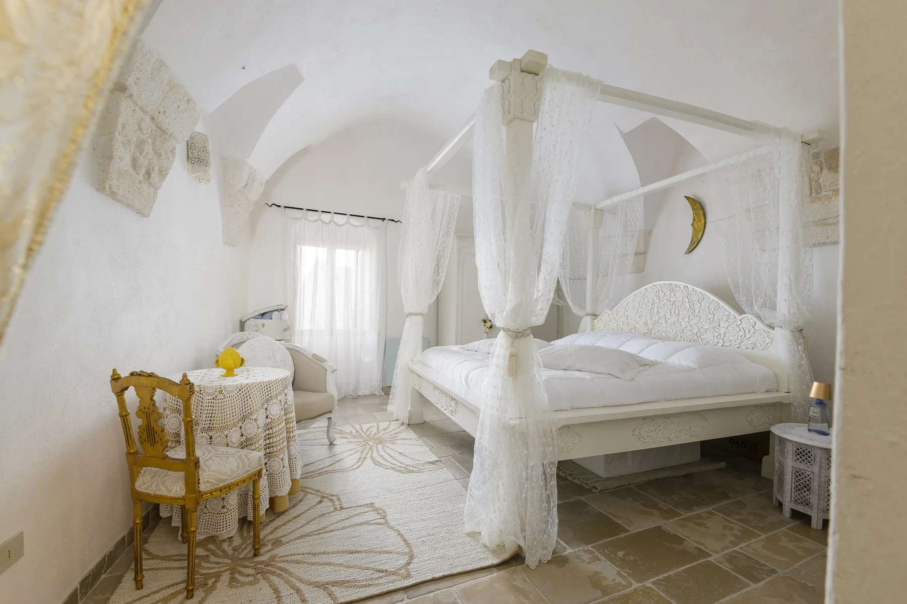 Un dormitorio luminoso con cama con dosel y cortinas, y una mesa redonda junto a la ventana.