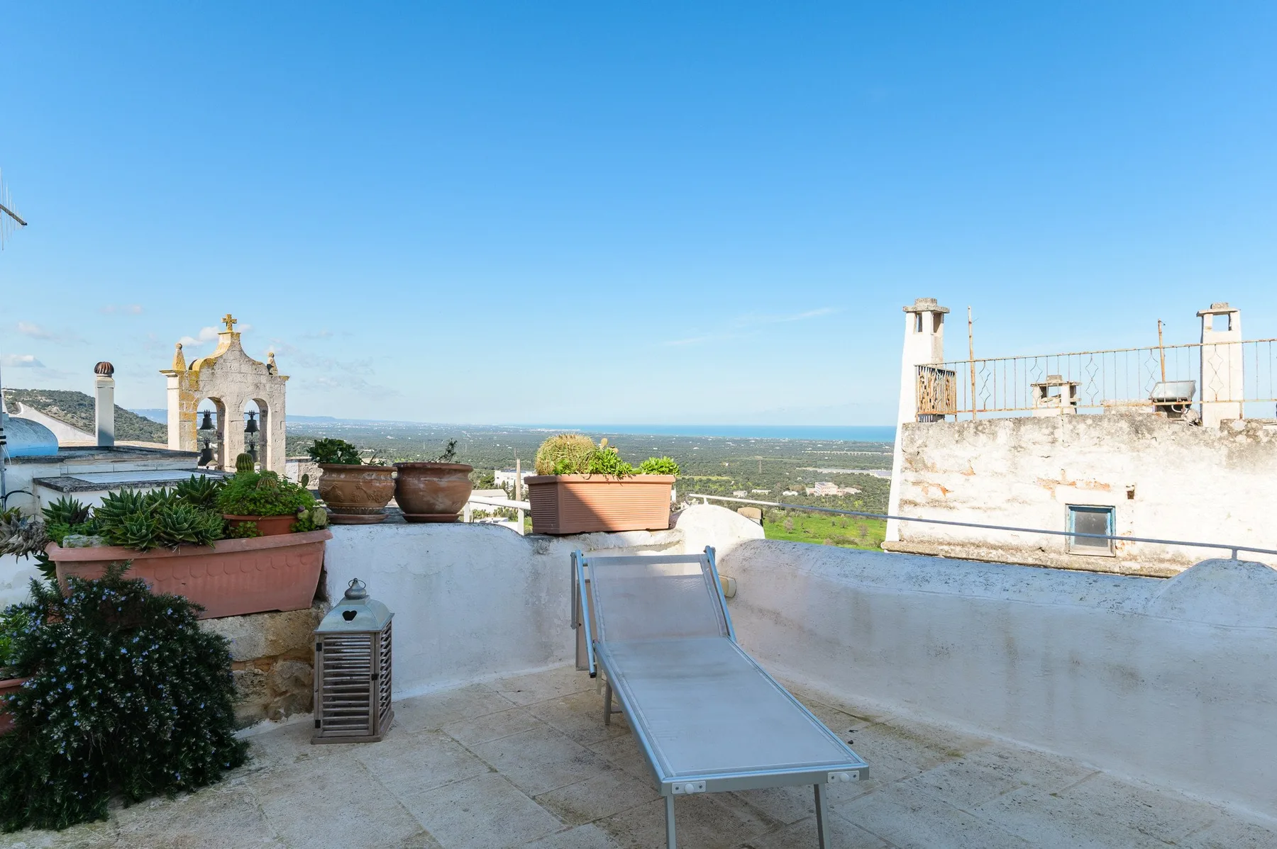 Una terraza en la azotea con una tumbona reclinable y plantas en macetas, con vistas al paisaje.