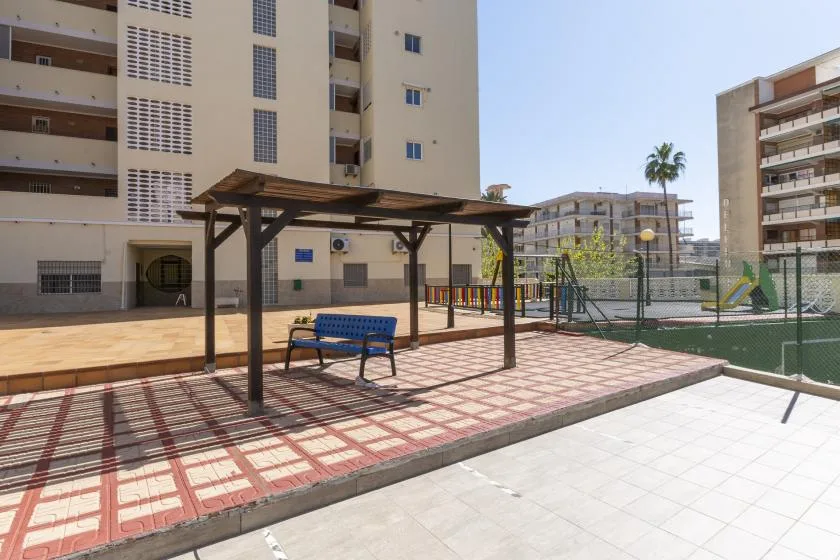 An outdoor courtyard with a shaded seating area and a fenced playground.
