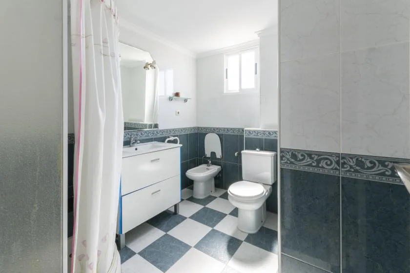 A bright bathroom with a vanity, toilet, and checkered floor.
