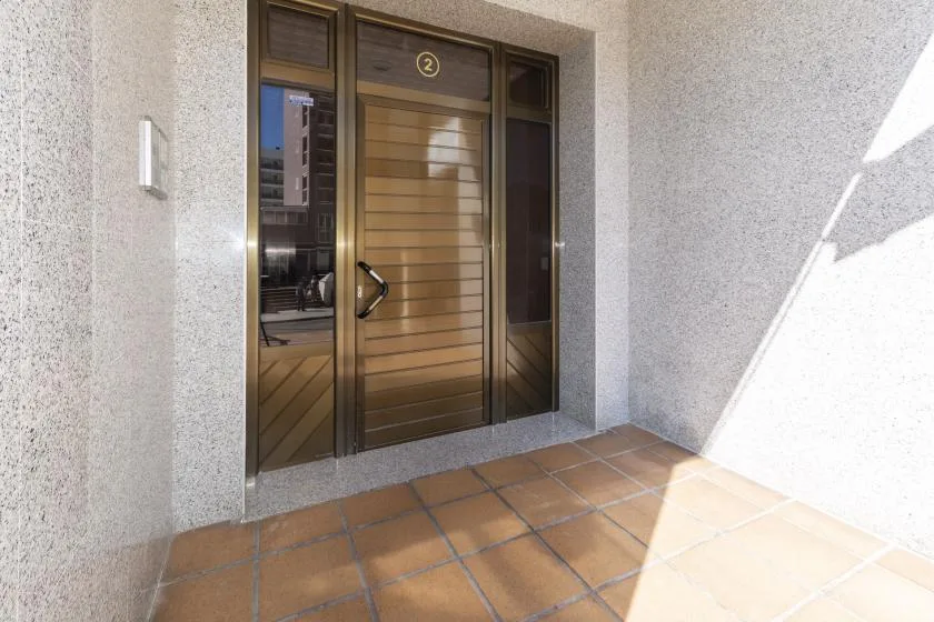 A wooden entrance door with glass side panels opens onto a tiled outdoor walkway.