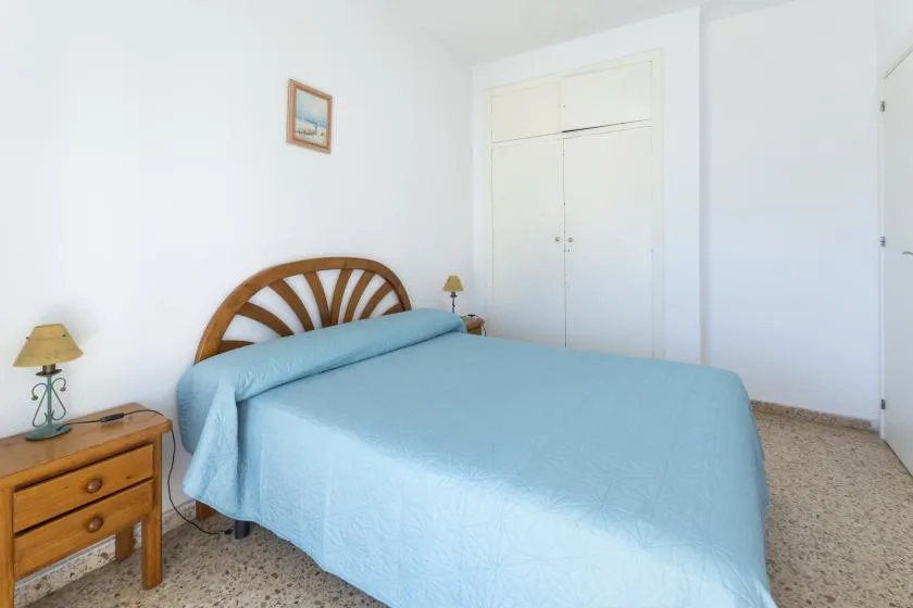A bedroom with a bed covered in a light blue bedspread and a wooden bedside table.