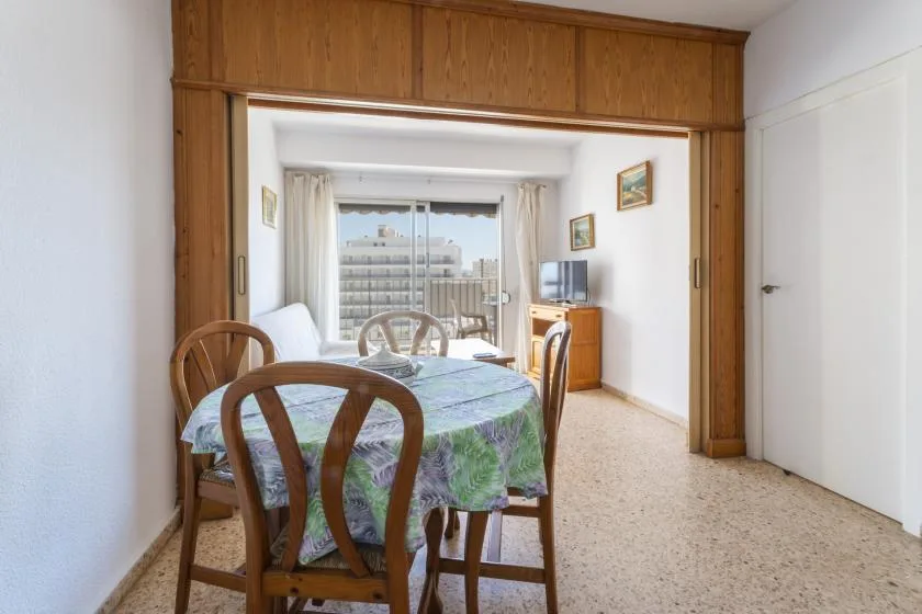 A dining area opens onto a bright sitting space with a balcony beyond.