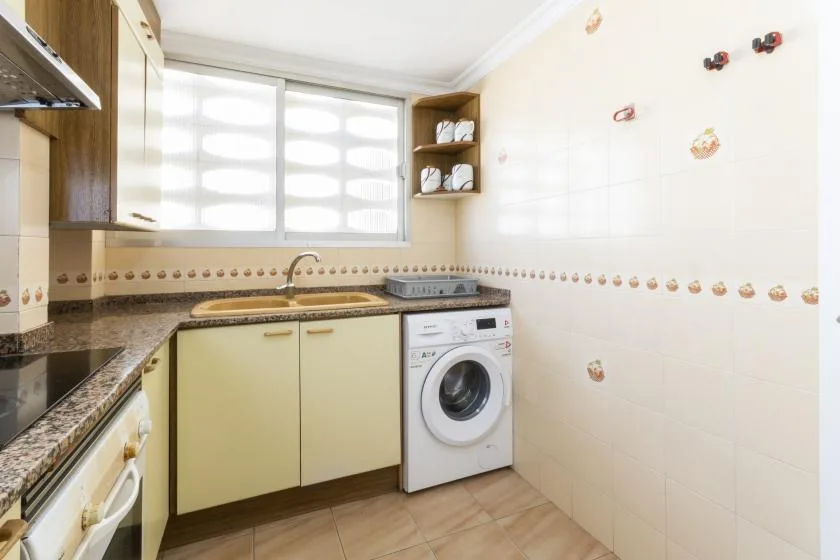 A bright kitchen with a corner countertop, sink, and washing machine.