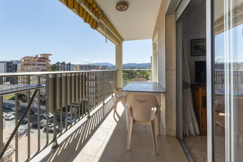 A covered balcony with outdoor seating overlooks nearby buildings and distant hills.