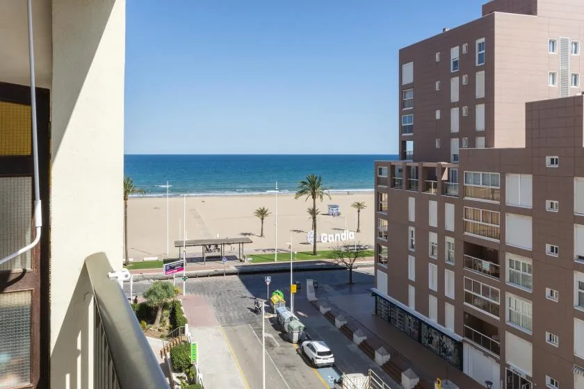 A view of the beach and ocean from a balcony, with buildings along the shore.