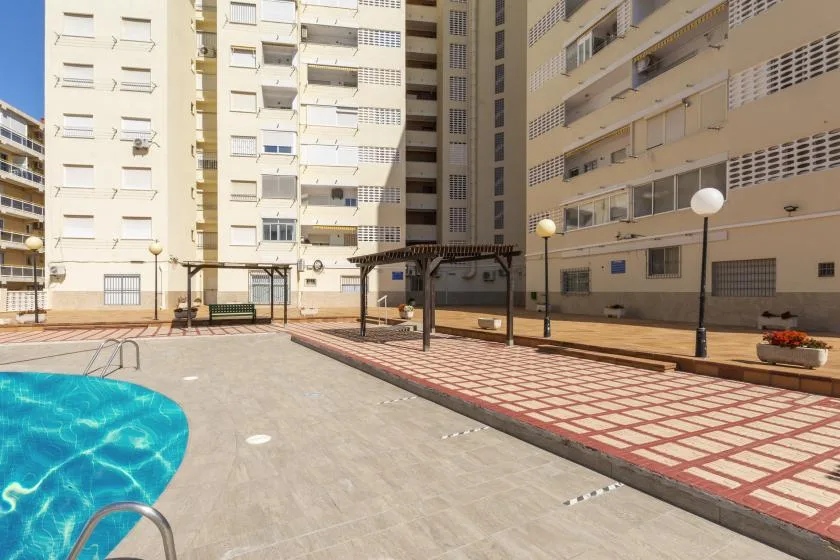 An outdoor pool courtyard between apartment buildings, with paved walkways and seating.