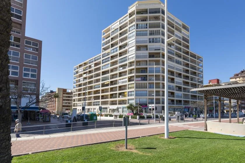 A tall multi-story building stands beside a paved walkway and grassy lawn.