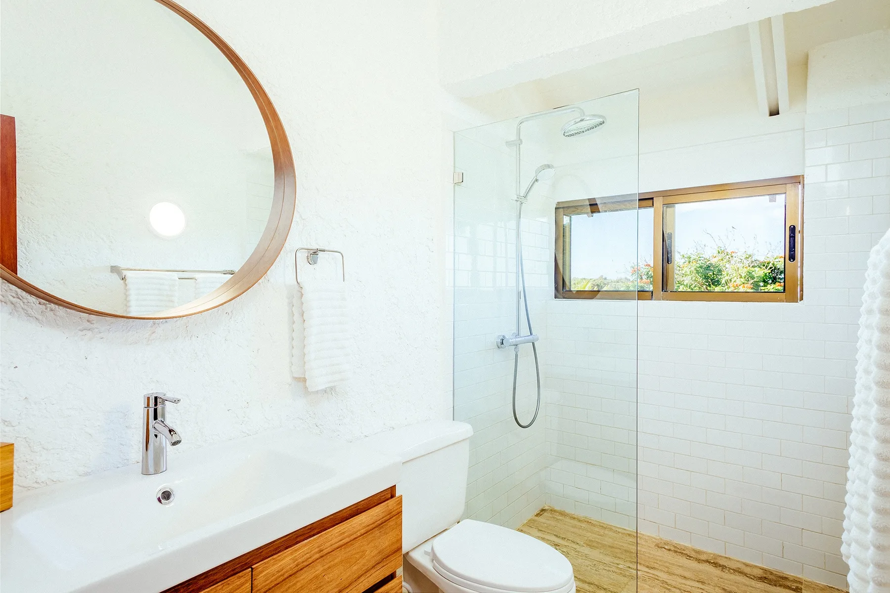 A bright bathroom with a sink, mirror, and glass shower.
