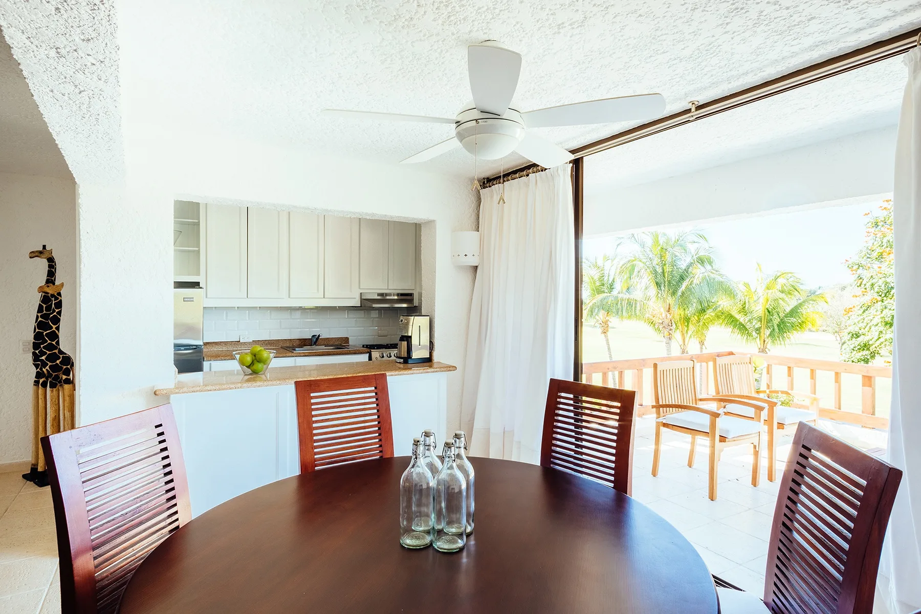 A dining area opens onto a bright balcony, with a compact kitchen behind it.
