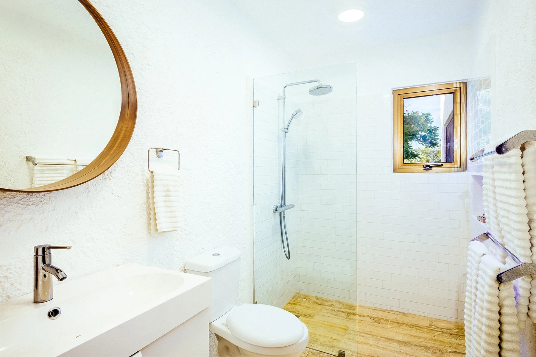 A bright bathroom with a sink, toilet, and glass shower screen.