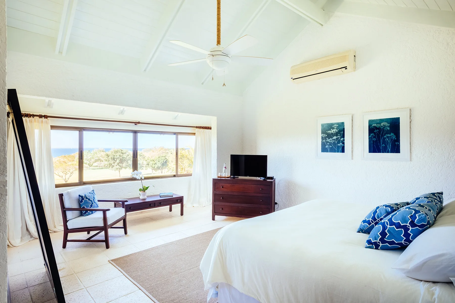 A bright bedroom with a large bed, seating area, and wide windows.