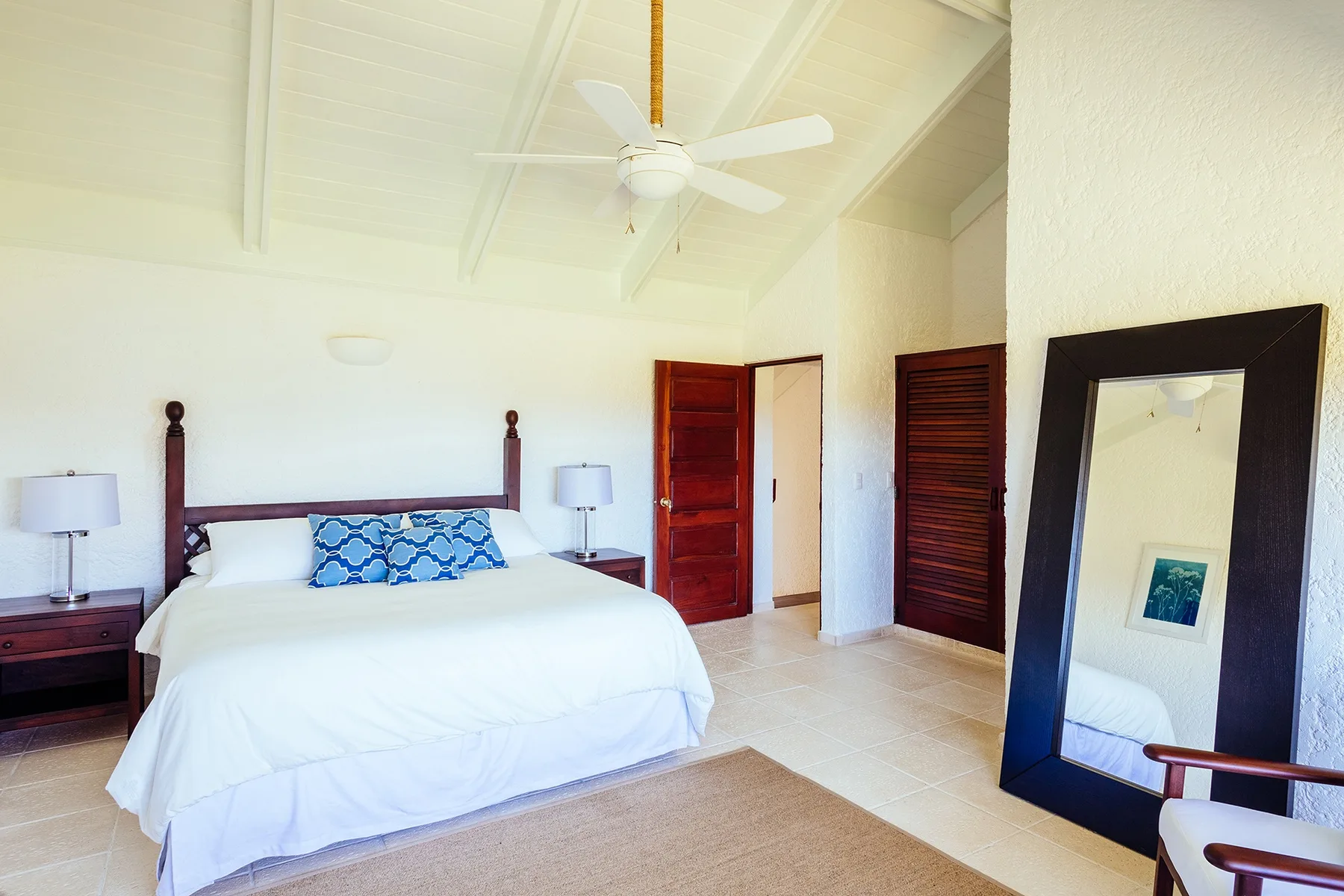 A bright bedroom with a neatly made bed and a large standing mirror.