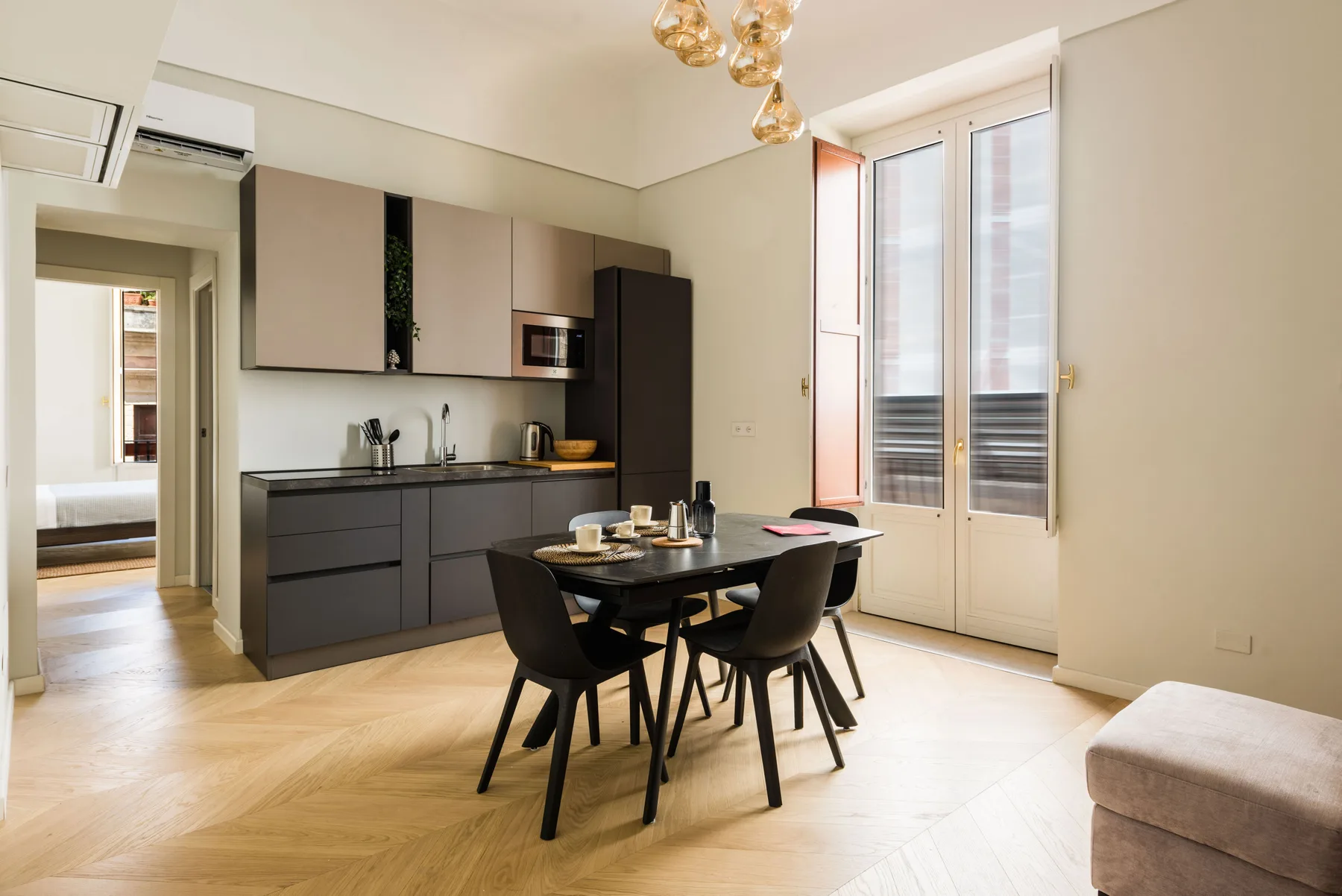 Una cocina moderna y zona de comedor con muebles oscuros y una mesa junto a las ventanas.