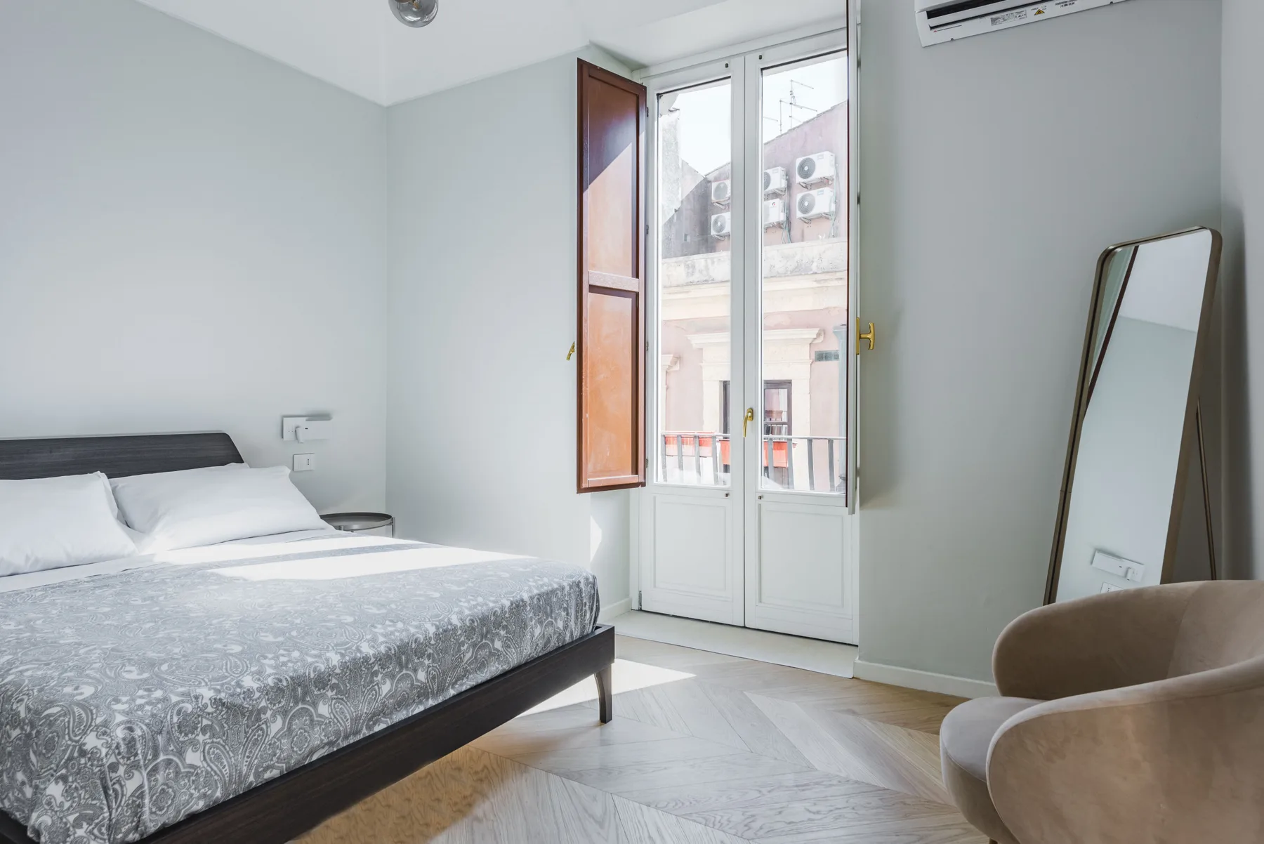 Un dormitorio con una cama junto a unas puertas acristaladas altas que dan a un balcón.
