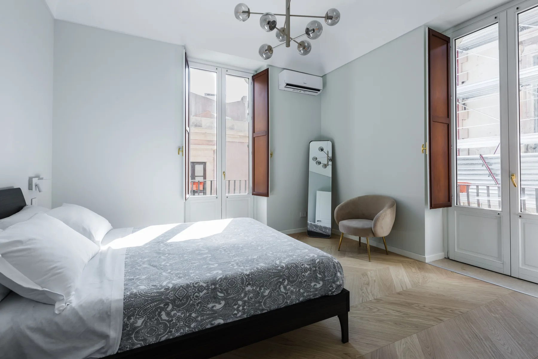 Un dormitorio luminoso con una cama y una silla junto a las ventanas.