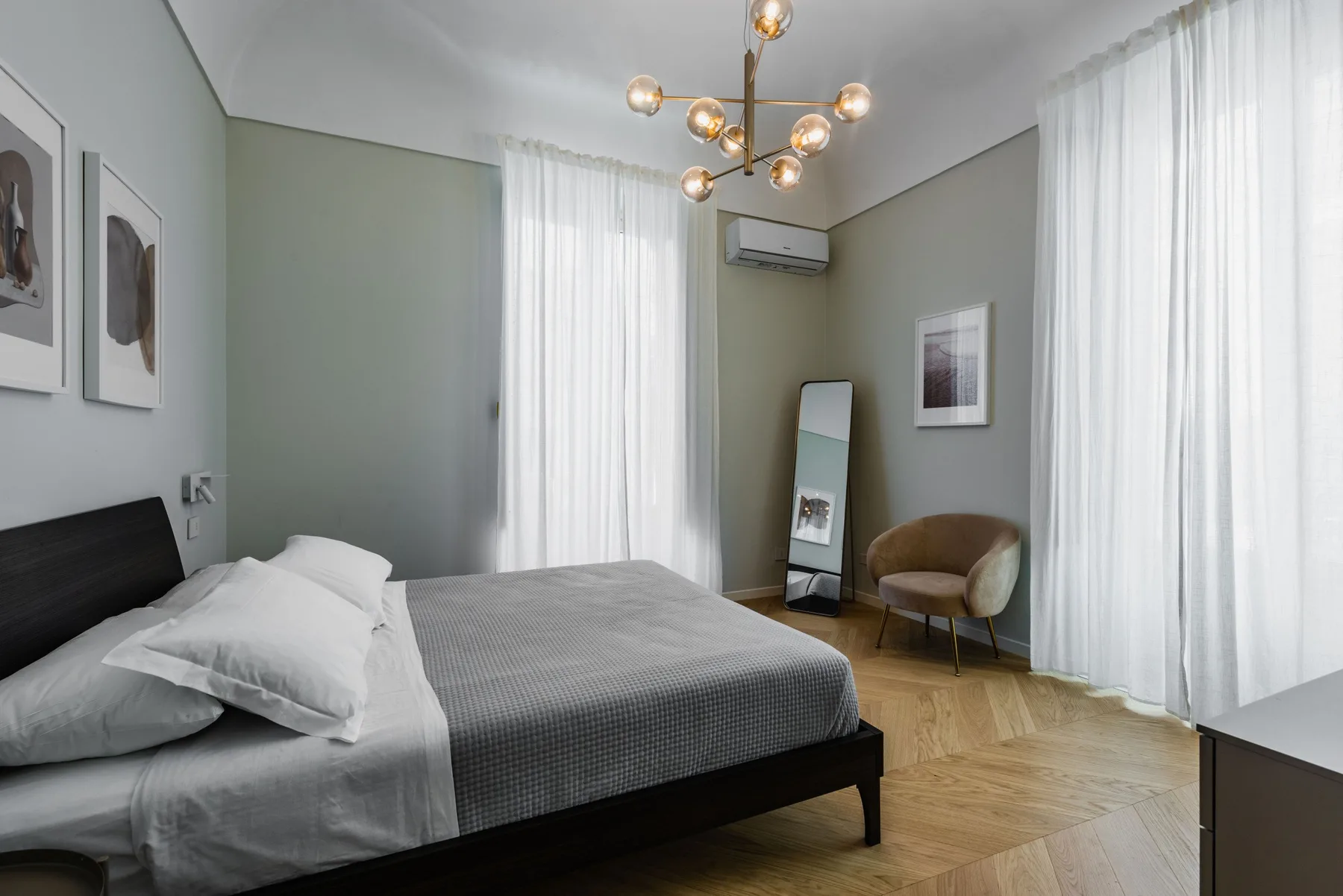 Dormitorio con una cama, una silla y cortinas largas.