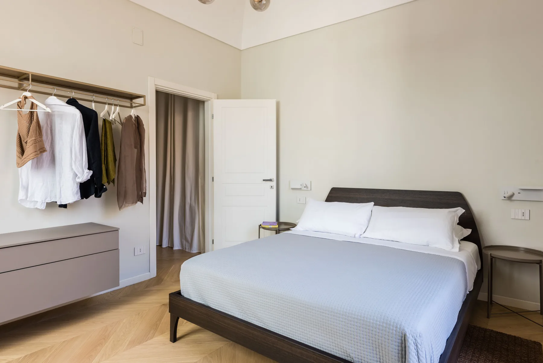 Un dormitorio con una cama y ropa colgada en un perchero abierto.