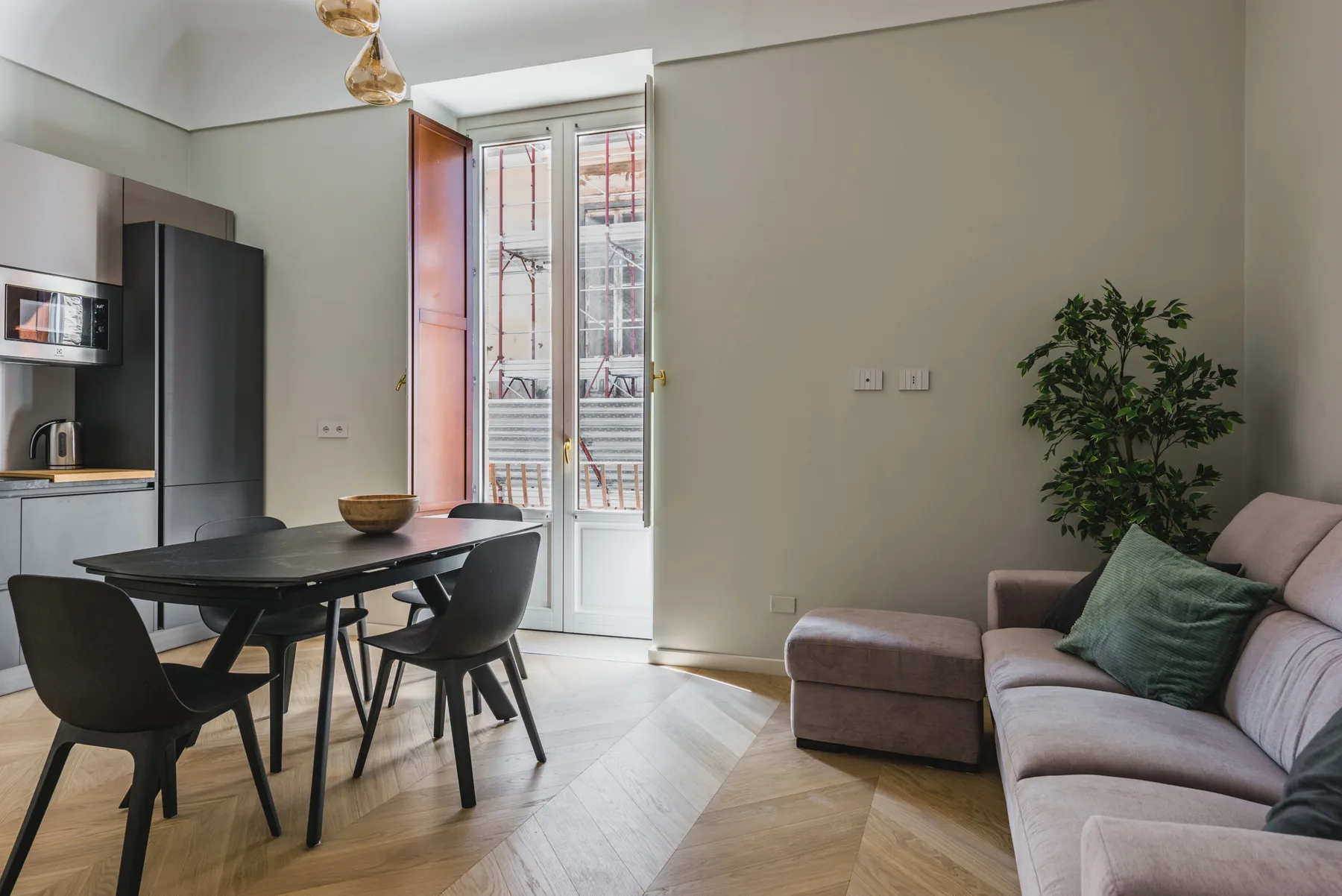 Un espacio de comedor y sala con una mesa y asientos junto a puertas de vidrio.
