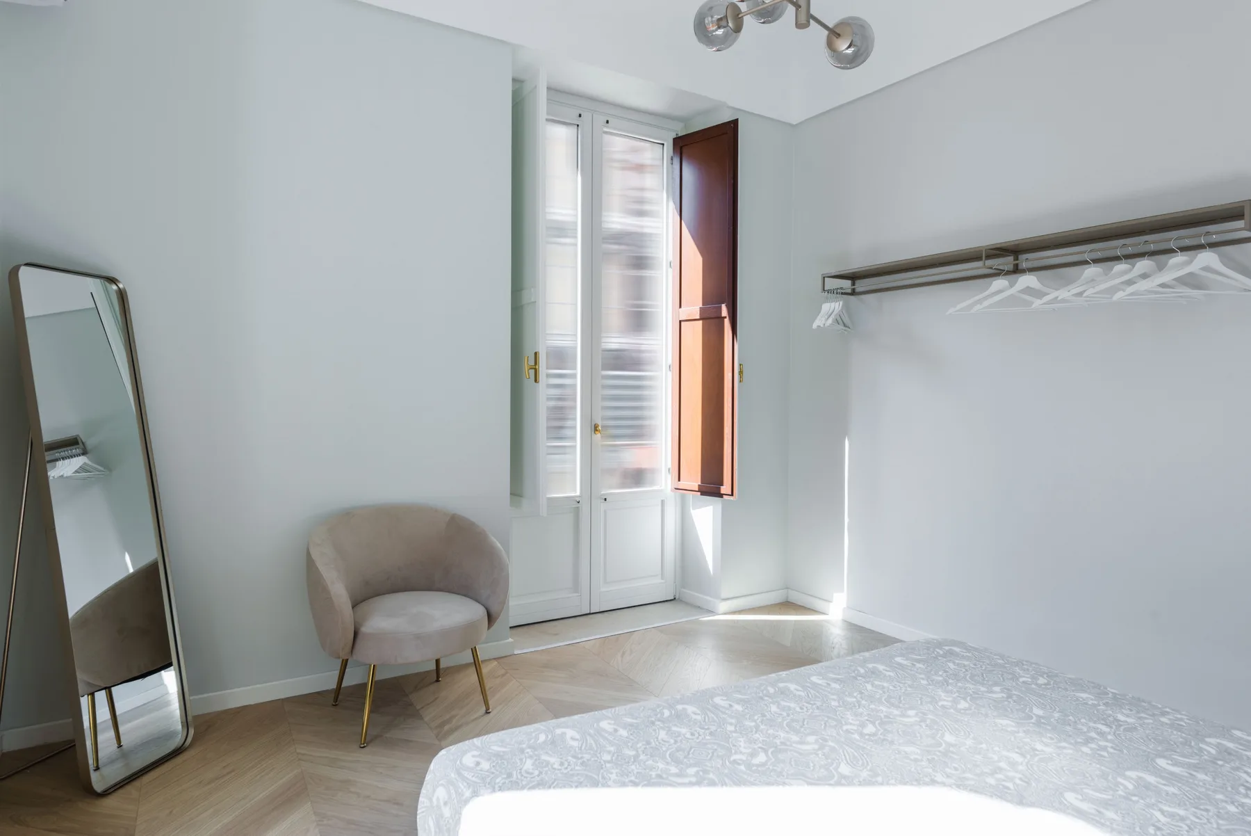 Un dormitorio luminoso con una cama, una silla y ventanas altas.