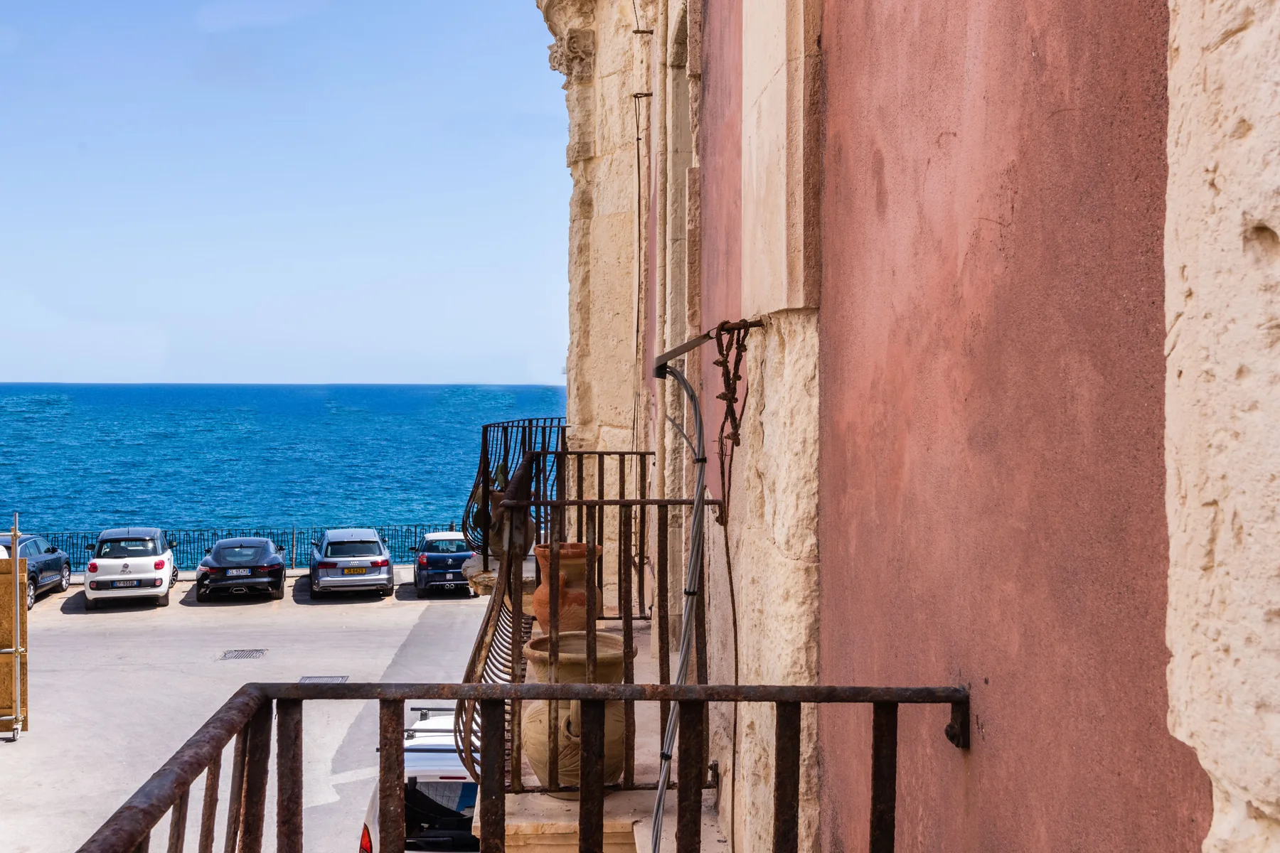 Una calle junto al mar da a aguas azules, con coches estacionados en la orilla.