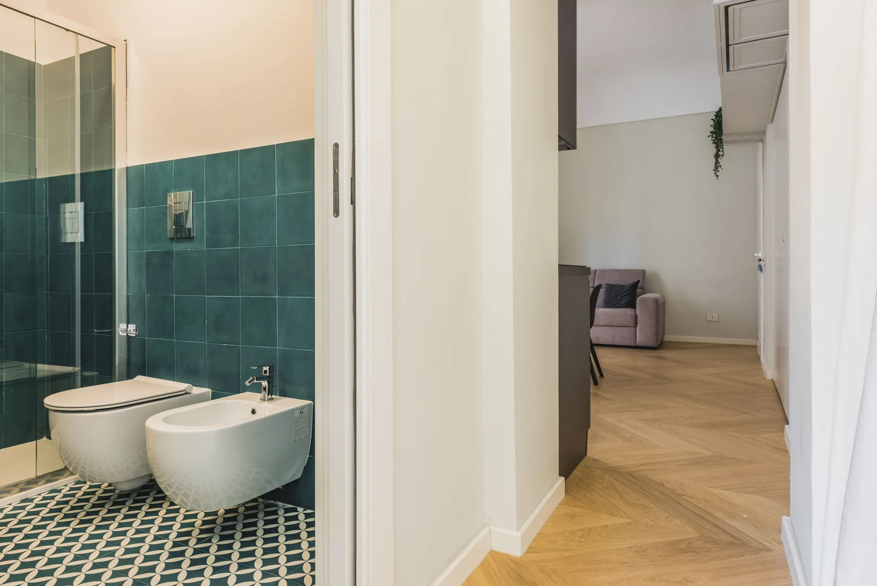 Un baño con ducha de vidrio y vista a una habitación contigua.