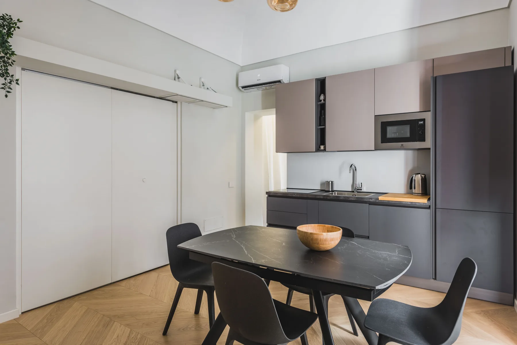 Un comedor con una mesa oscura y una cocina compacta al fondo.