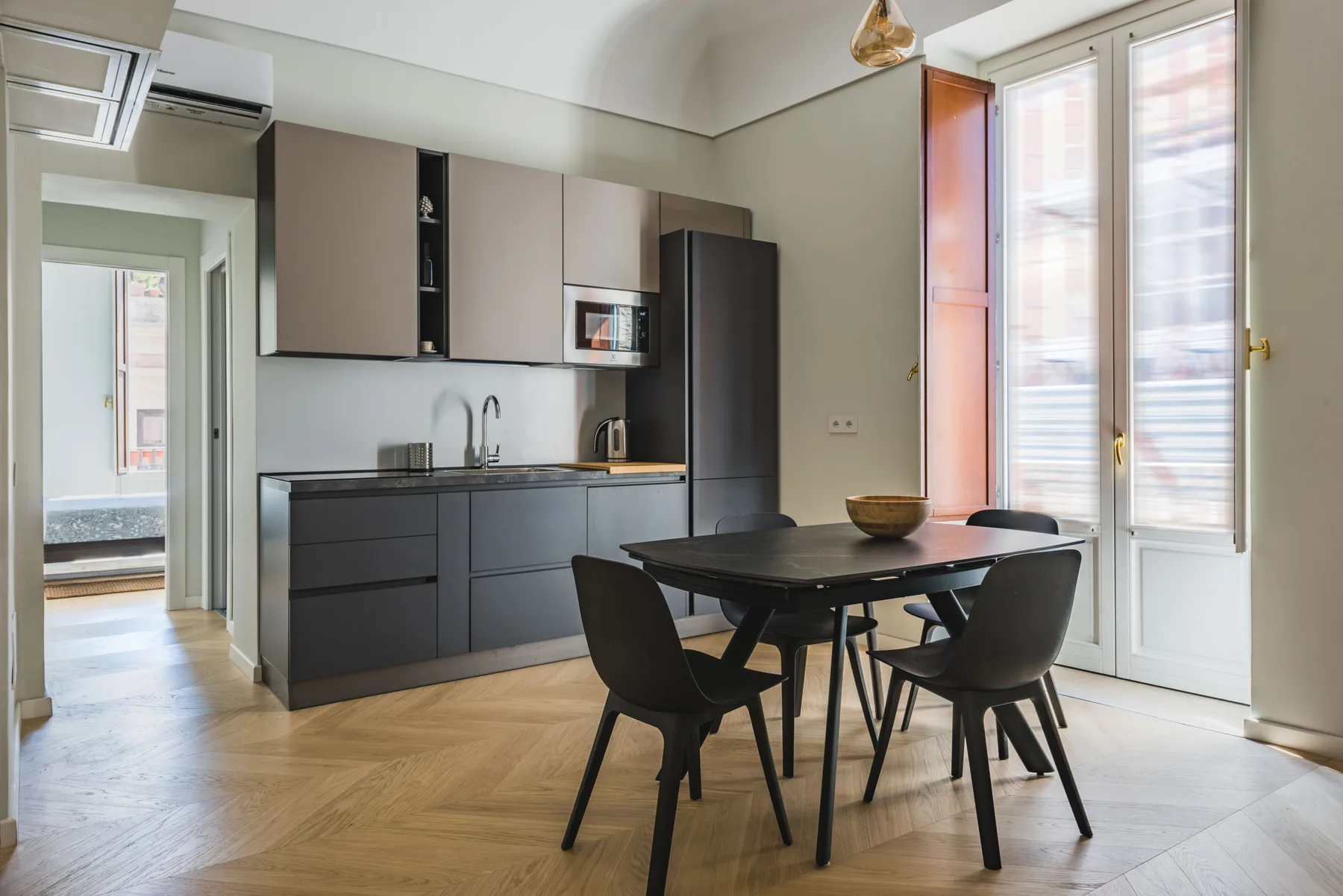 Una cocina moderna y zona de comedor con armarios oscuros y una mesa junto a las ventanas.