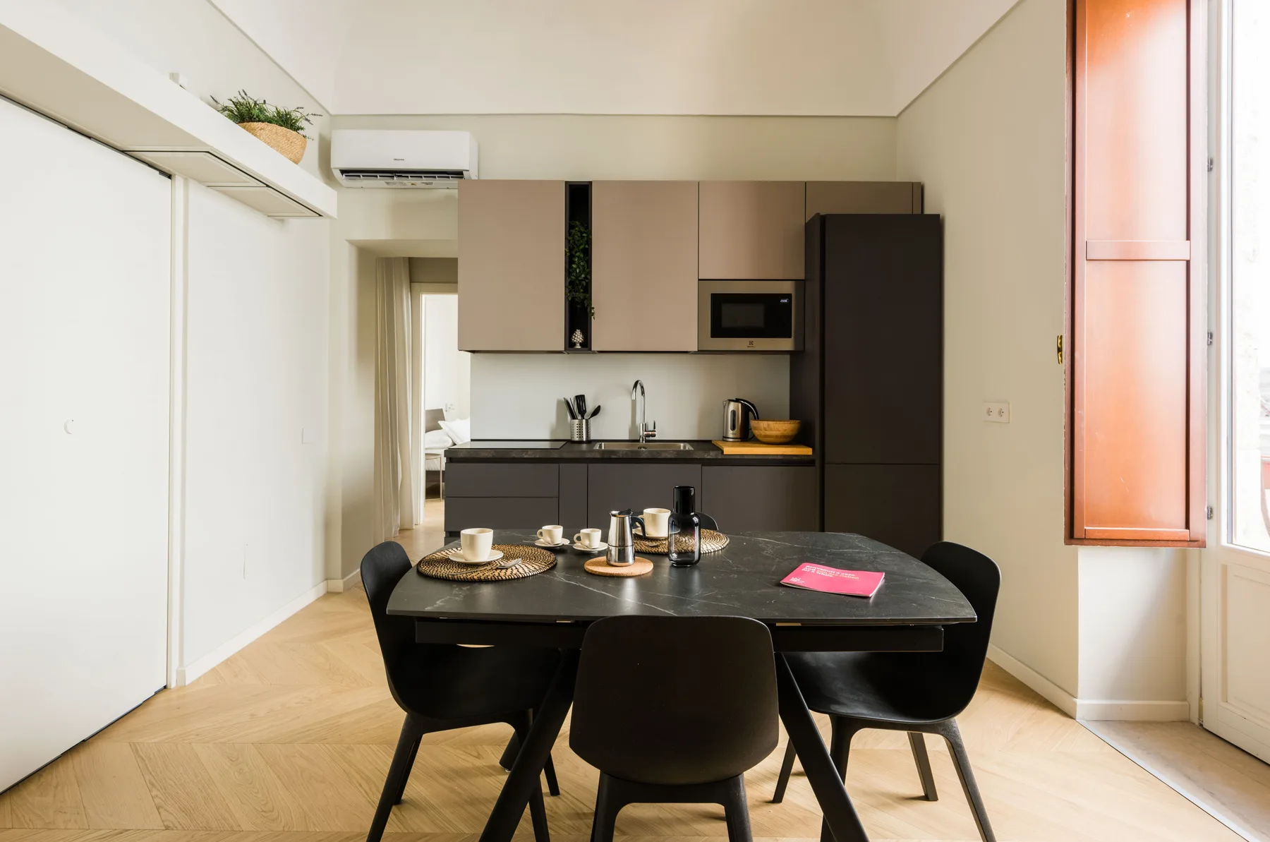 Comedor con una mesa oscura y sillas junto a una cocina compacta.
