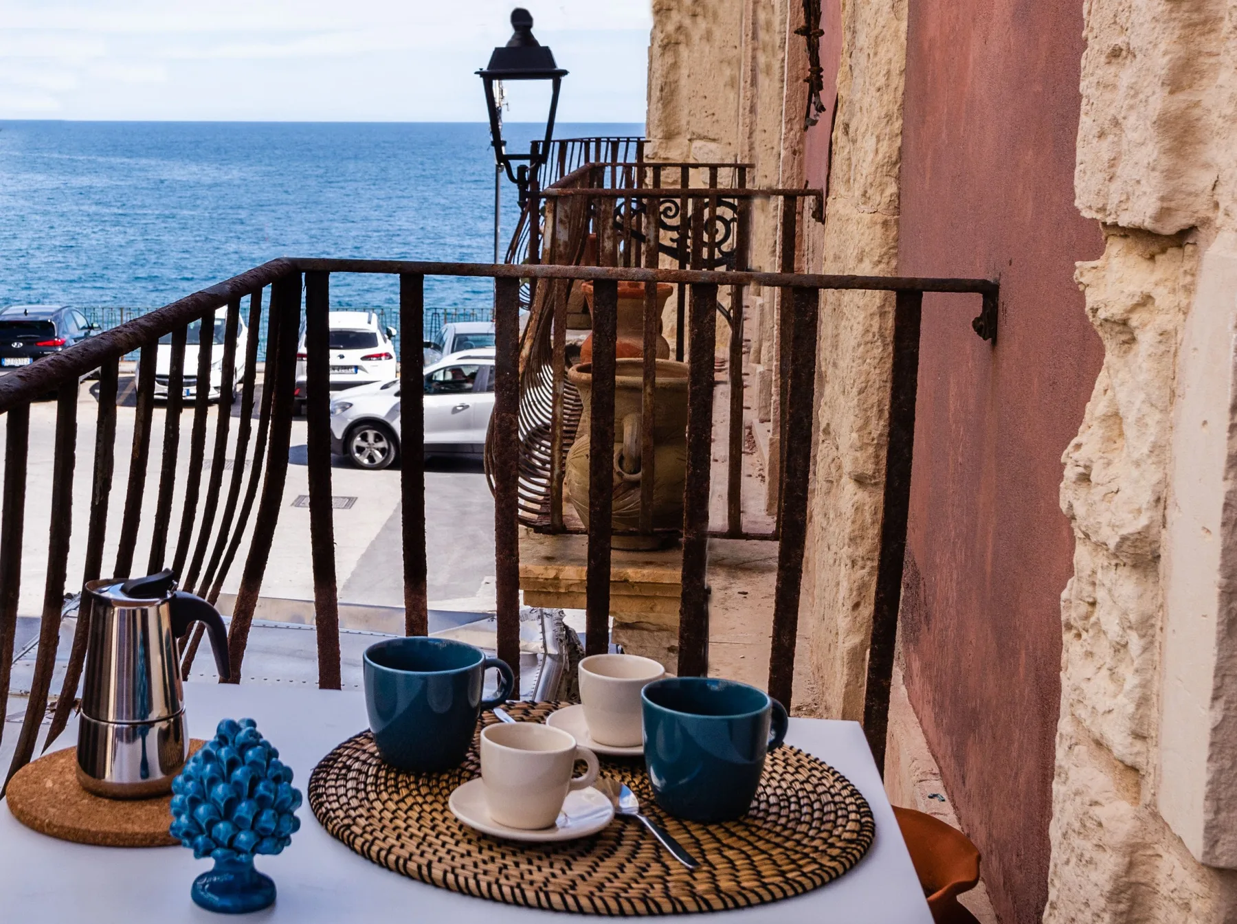 Un balcón junto al mar con tazas de café sobre una mesa junto a la barandilla.