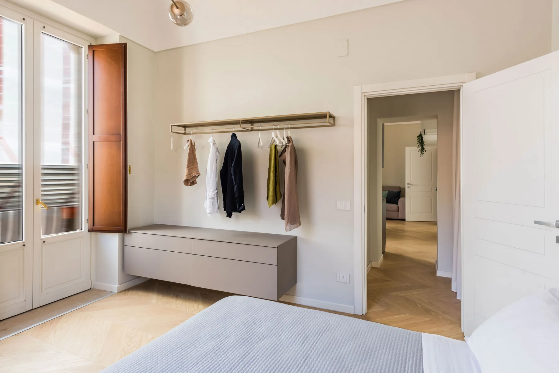 Un dormitorio luminoso con una cómoda baja y ropa colgada en un perchero de pared.