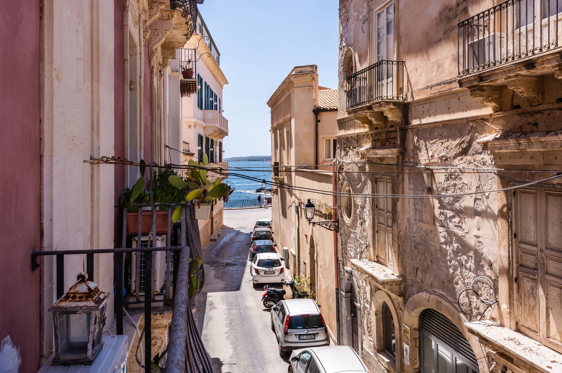 Una calle estrecha pasa entre edificios antiguos hacia el mar, con coches estacionados.
