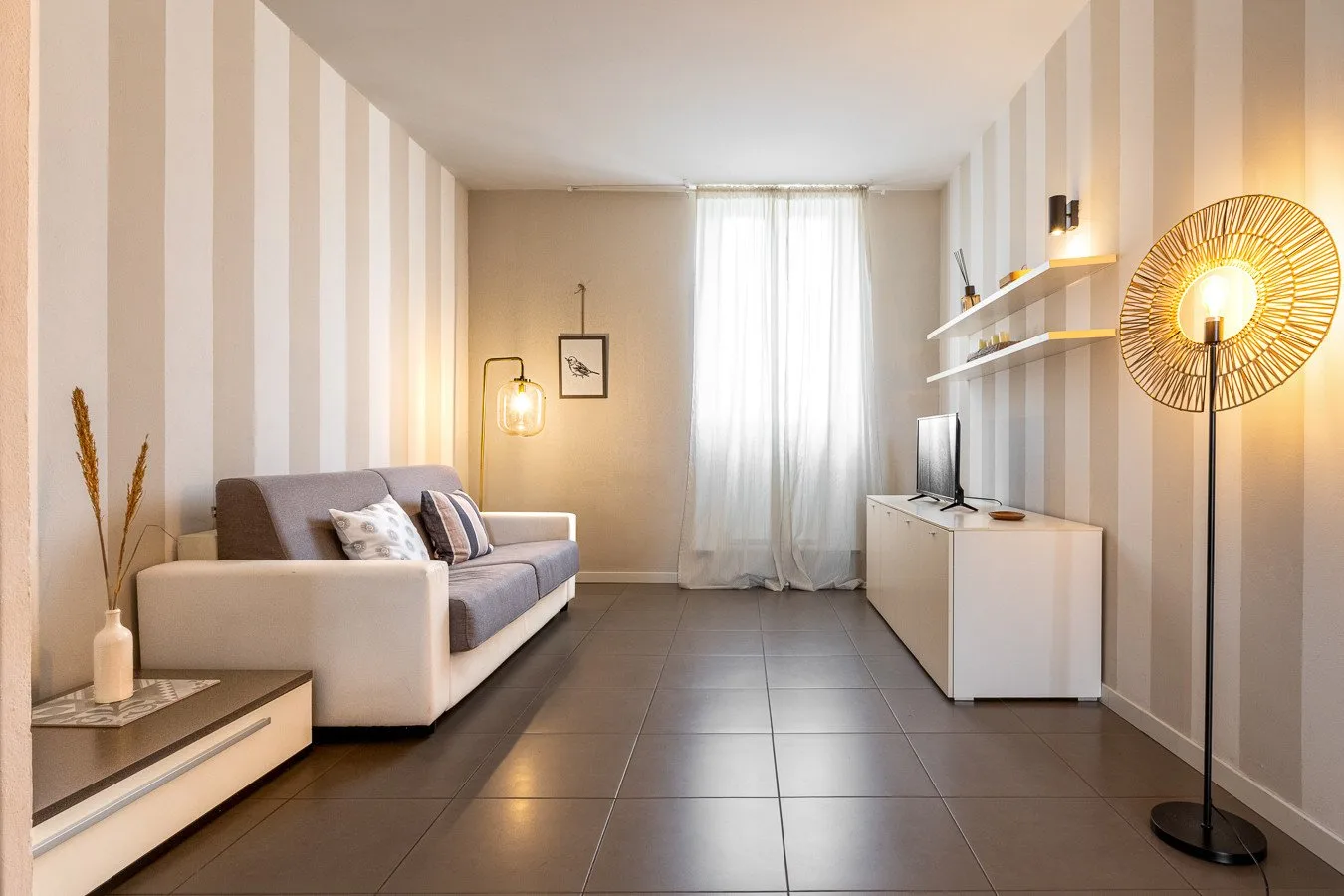 Una sala de estar con asientos, un televisor y una ventana luminosa.