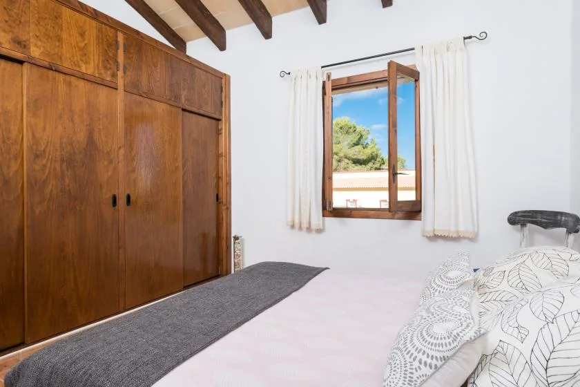 A bedroom with a bed, a large wooden wardrobe, and an open window.