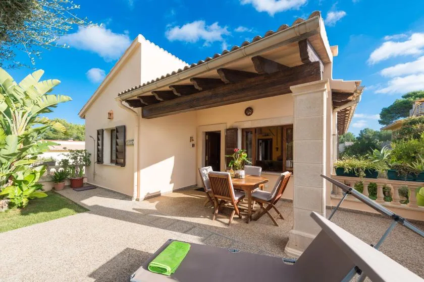 A sunny outdoor patio with a wooden dining table beneath a covered terrace.