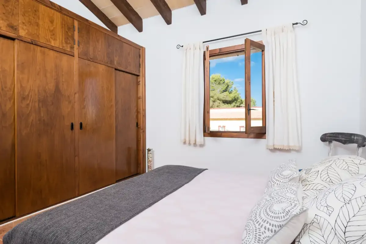 A bedroom with a bed, wooden wardrobe, and window overlooking greenery.