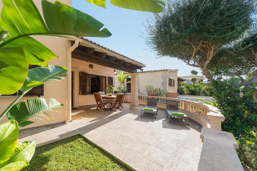 A sunny outdoor patio with a dining table, lounge seating, and leafy plants.