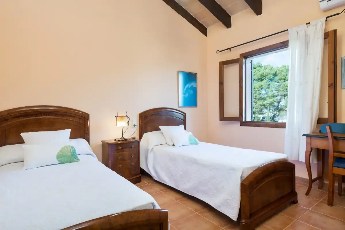 A bedroom with two beds and a window overlooking greenery.