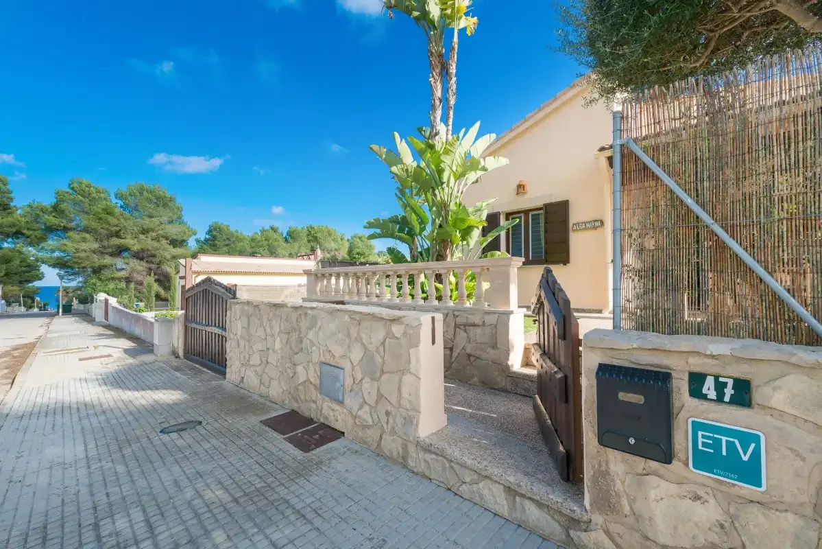 A paved sidewalk runs beside a low stone wall and house entrance.