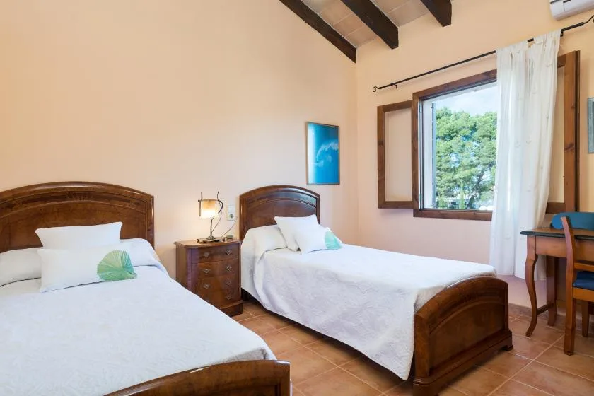 A bedroom with two beds, a bedside table, and a window with white curtains.