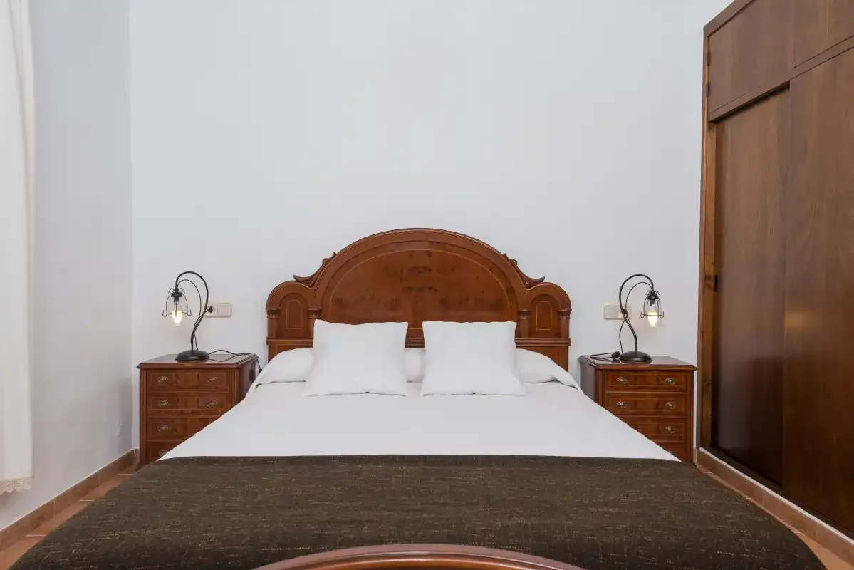 A bedroom with a bed, wooden headboard, and matching bedside tables.